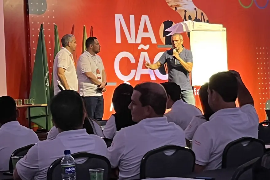 Evandro Lopes no palco de um evento corporativo, de microfone, diante de uma plateia sentada